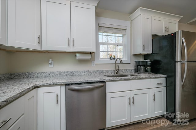 kitchen featuring white cabinetry, light stone countertops, appliances with stainless steel finishes, and a sink