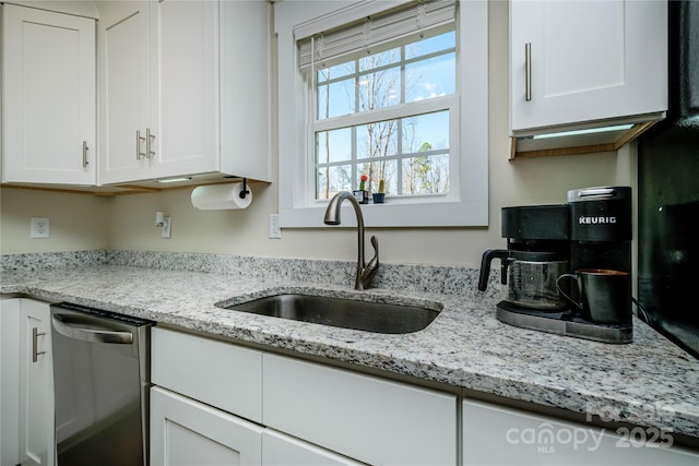 kitchen featuring stainless steel dishwasher, light stone counters, white cabinetry, and a sink