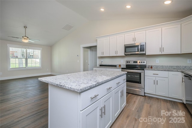 kitchen with wood finished floors, a center island, appliances with stainless steel finishes, white cabinets, and lofted ceiling