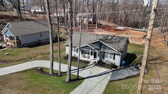 view of front of property with covered porch, concrete driveway, a front lawn, and roof with shingles