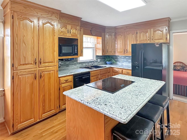 kitchen with black appliances, a sink, a kitchen breakfast bar, backsplash, and light wood-style floors