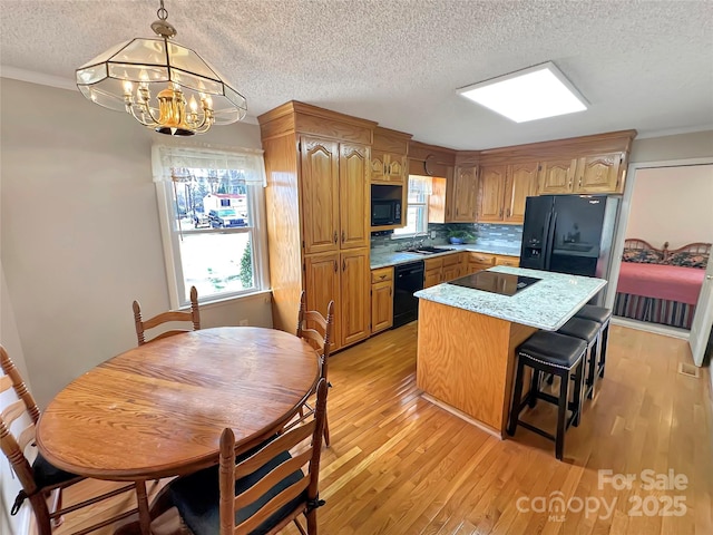 kitchen featuring light wood-style flooring, a sink, black appliances, a notable chandelier, and a center island