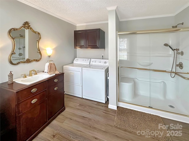 clothes washing area with washing machine and dryer, laundry area, light wood-style flooring, a textured ceiling, and a sink