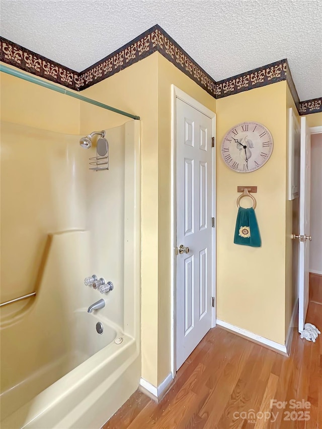 full bath with baseboards, a textured ceiling, shower / washtub combination, and wood finished floors