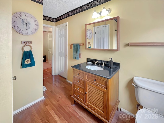 bathroom featuring vanity, wood finished floors, baseboards, a textured ceiling, and toilet