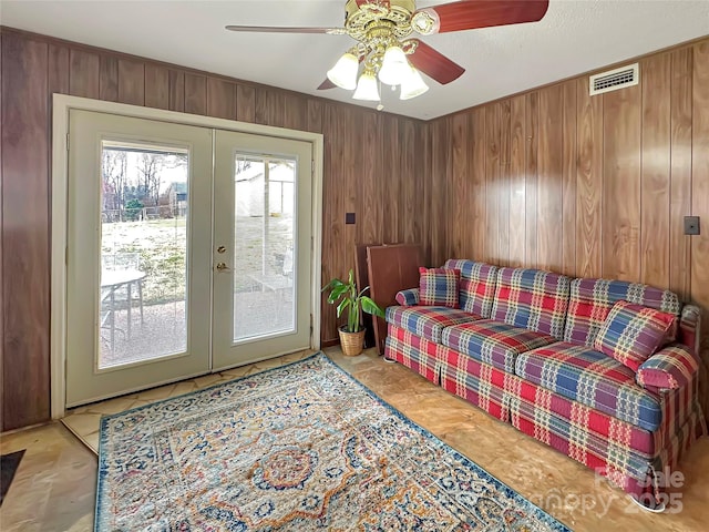 living area featuring a ceiling fan, wooden walls, french doors, and visible vents