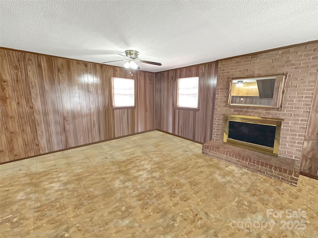 unfurnished living room featuring wooden walls, baseboards, ceiling fan, a fireplace, and a textured ceiling