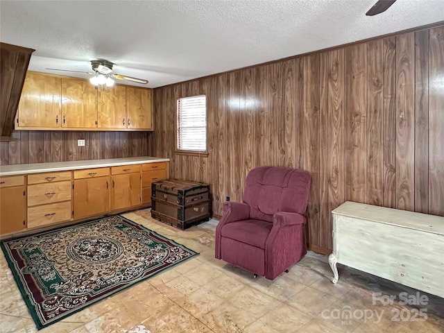 living area with a textured ceiling, light floors, ceiling fan, and wood walls