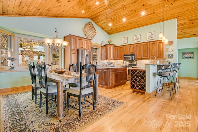 kitchen with a kitchen bar, light wood-style floors, appliances with stainless steel finishes, brown cabinetry, and wood ceiling