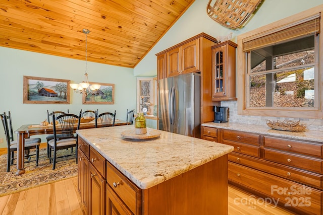 kitchen featuring light stone countertops, brown cabinetry, a kitchen island, freestanding refrigerator, and wooden ceiling