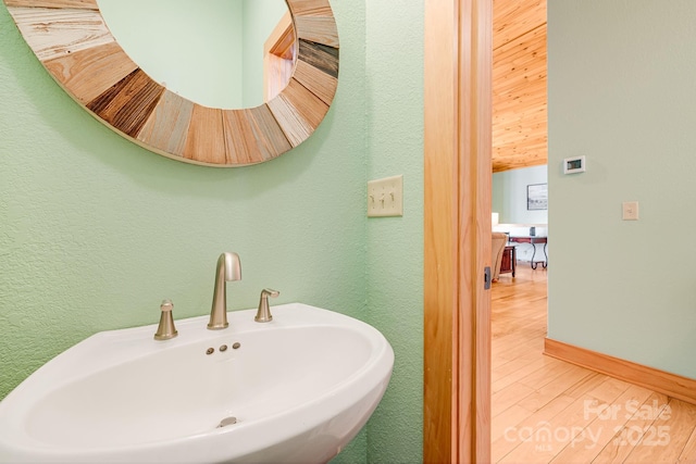 bathroom with baseboards, wood finished floors, a textured wall, and a sink