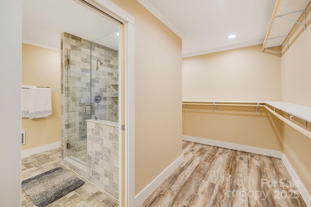 full bath featuring wood finished floors, a shower stall, crown molding, baseboards, and a spacious closet