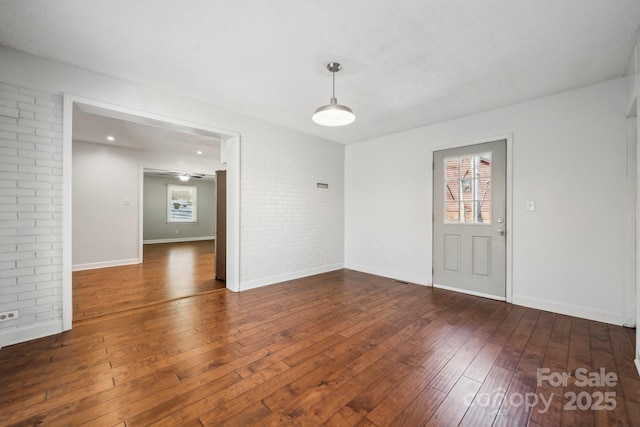 empty room featuring hardwood / wood-style floors, a healthy amount of sunlight, baseboards, and brick wall