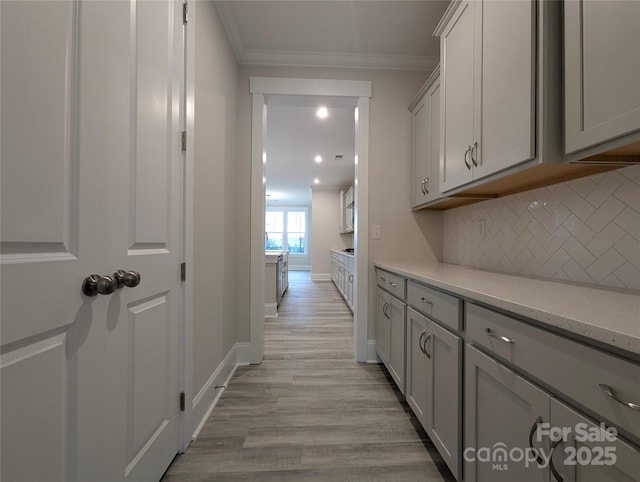 hall featuring crown molding, baseboards, and light wood-type flooring