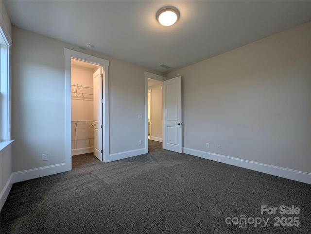 unfurnished bedroom with visible vents, baseboards, a spacious closet, and dark carpet