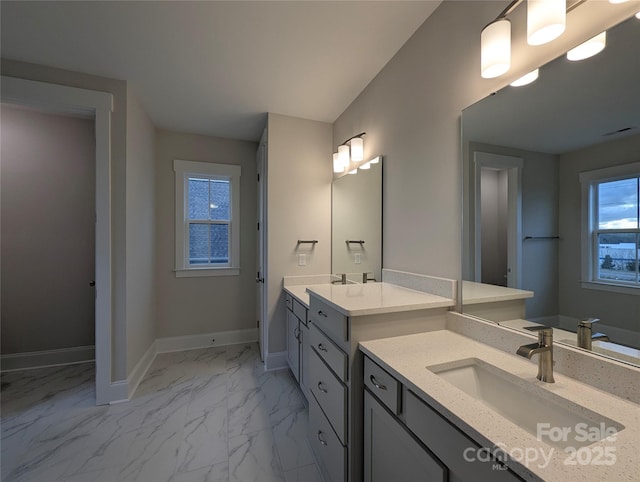 bathroom featuring two vanities, baseboards, marble finish floor, and a sink