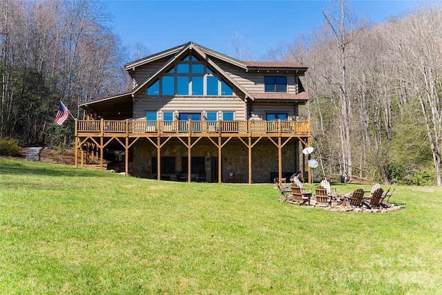 back of house featuring a wooden deck, stone siding, a fire pit, and a lawn