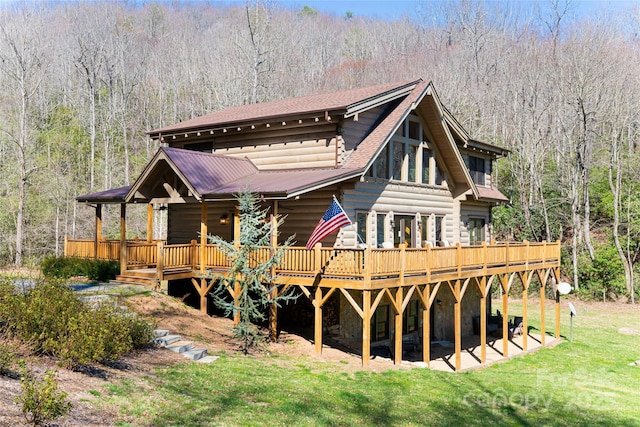 back of house featuring stone siding, a lawn, and a view of trees