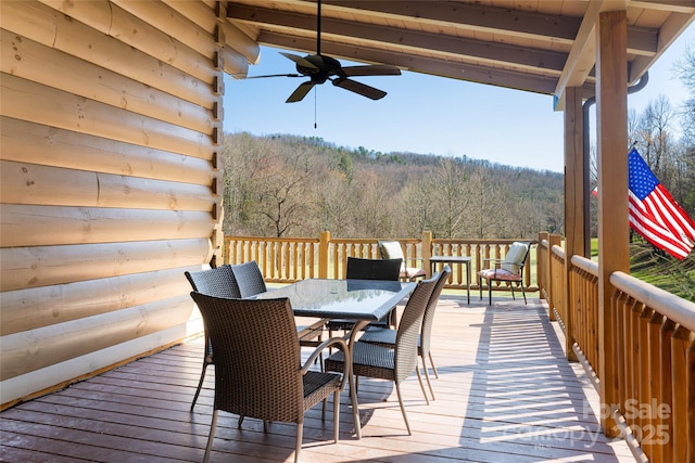 wooden terrace featuring a forest view, outdoor dining area, and a ceiling fan