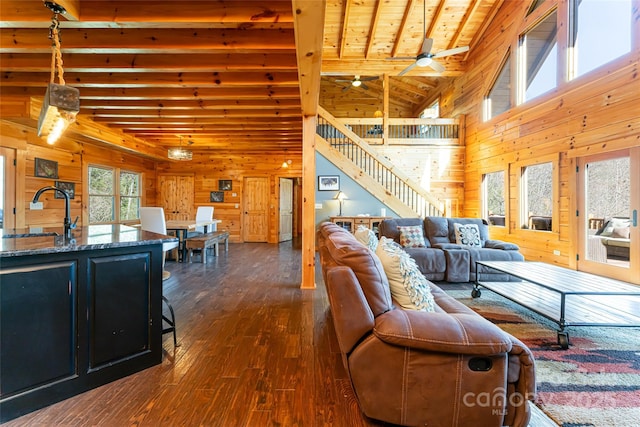 living area with beam ceiling, wooden walls, dark wood finished floors, and stairs