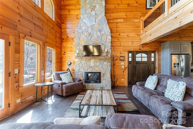 living area with hardwood / wood-style floors, a stone fireplace, wooden walls, and a towering ceiling