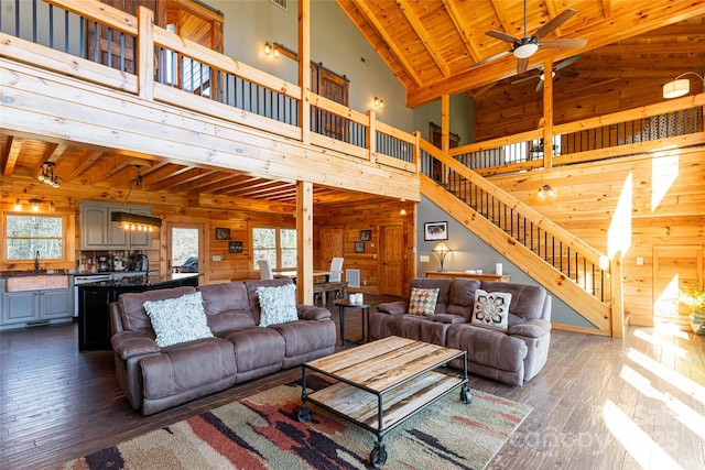 living room featuring dark wood-style floors, wood walls, wood ceiling, ceiling fan, and stairs