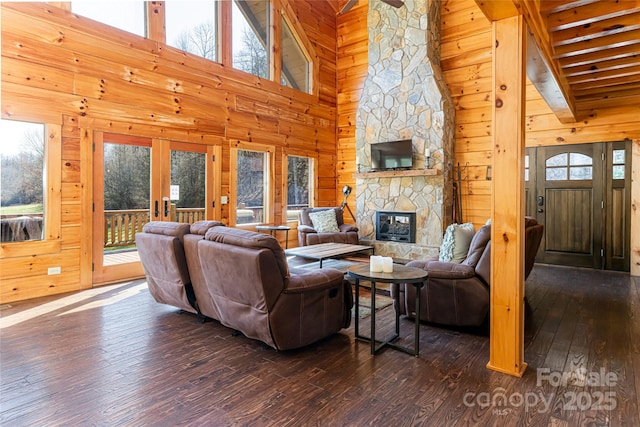 living room with high vaulted ceiling, french doors, a stone fireplace, wood walls, and dark wood-style flooring