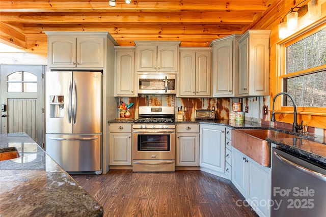 kitchen featuring beam ceiling, dark stone countertops, a sink, dark wood finished floors, and appliances with stainless steel finishes