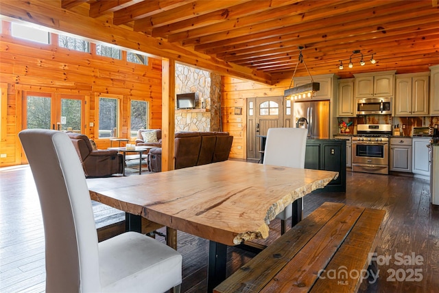 dining area with dark wood finished floors, beam ceiling, wood walls, and track lighting