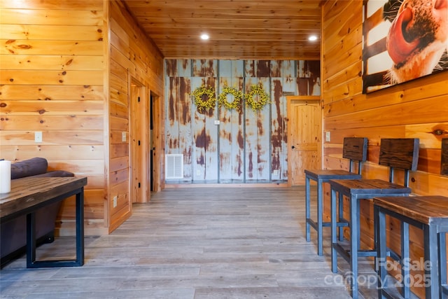 hallway with visible vents, wood finished floors, wooden walls, and wooden ceiling