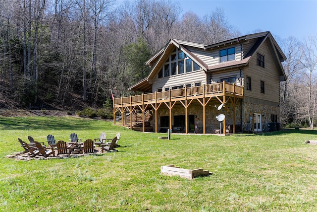 rear view of house with a wooded view, an outdoor fire pit, a lawn, a deck, and stone siding