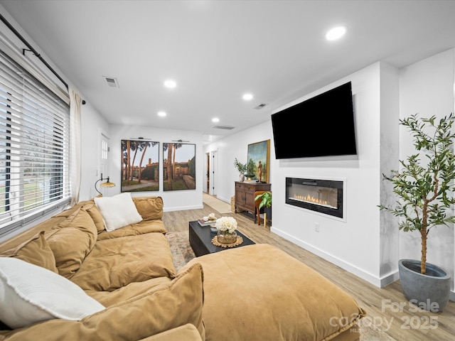 living room featuring a glass covered fireplace, light wood-style flooring, recessed lighting, and visible vents