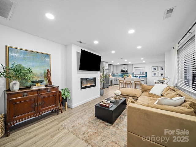 living area featuring visible vents, recessed lighting, light wood-style floors, and a glass covered fireplace