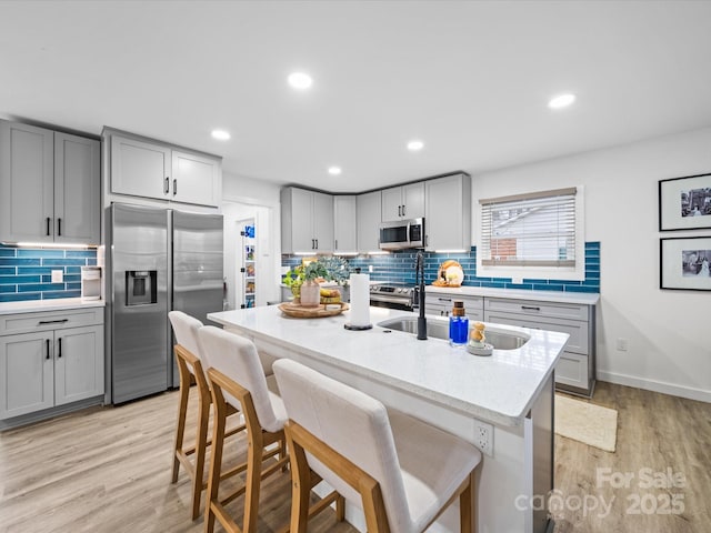 kitchen featuring a breakfast bar, light wood-style flooring, gray cabinetry, and stainless steel appliances