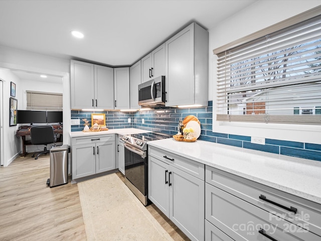 kitchen featuring recessed lighting, light wood-style floors, appliances with stainless steel finishes, decorative backsplash, and light stone countertops