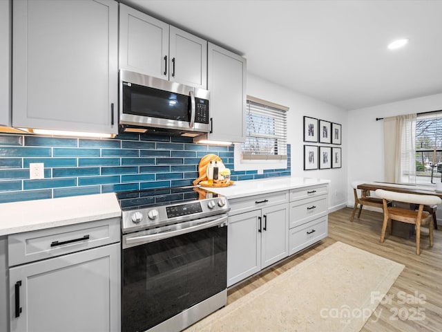 kitchen with light wood-style floors, stainless steel appliances, tasteful backsplash, and light countertops