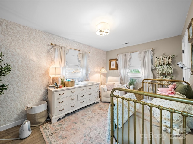 bedroom with visible vents, baseboards, wood finished floors, and wallpapered walls