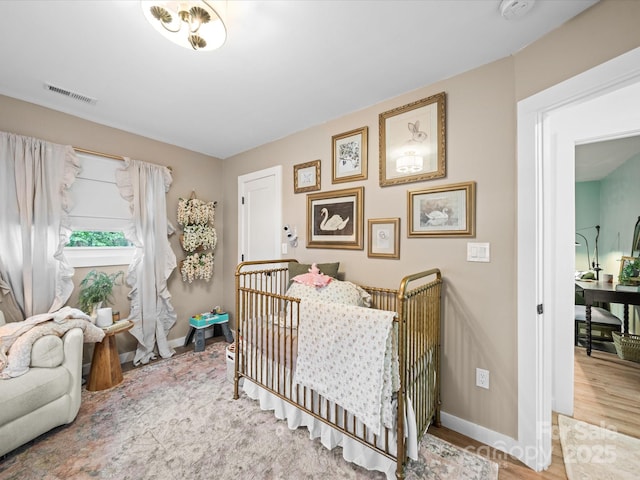 bedroom featuring a crib, wood finished floors, visible vents, and baseboards