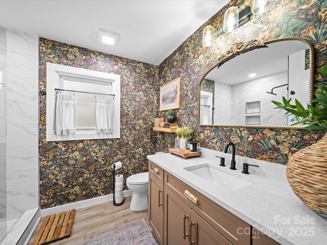 bathroom featuring toilet, wood finished floors, baseboards, walk in shower, and vanity