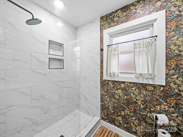 bathroom with a tile shower, wallpapered walls, and baseboards