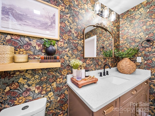 half bathroom featuring toilet, vanity, and wallpapered walls