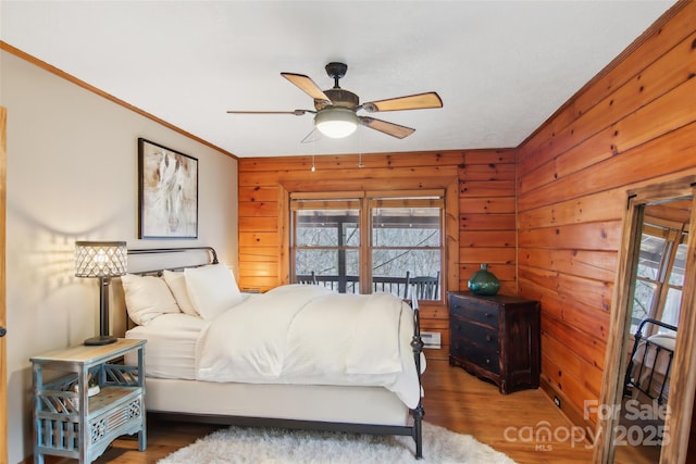 bedroom with ceiling fan, wooden walls, and wood finished floors