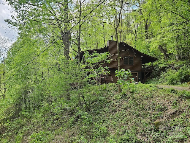 view of side of property featuring a view of trees, a chimney, and a wooden deck