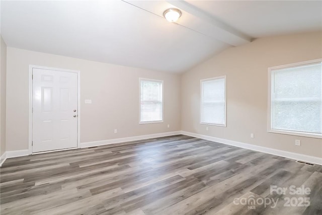 unfurnished room with visible vents, vaulted ceiling with beams, wood finished floors, and baseboards