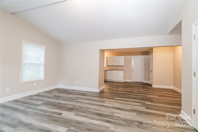 unfurnished living room featuring vaulted ceiling, wood finished floors, and baseboards