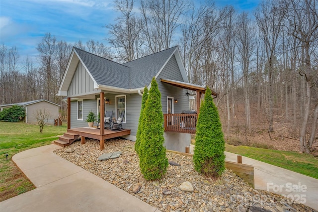 view of side of property featuring a lawn, a ceiling fan, board and batten siding, covered porch, and a shingled roof