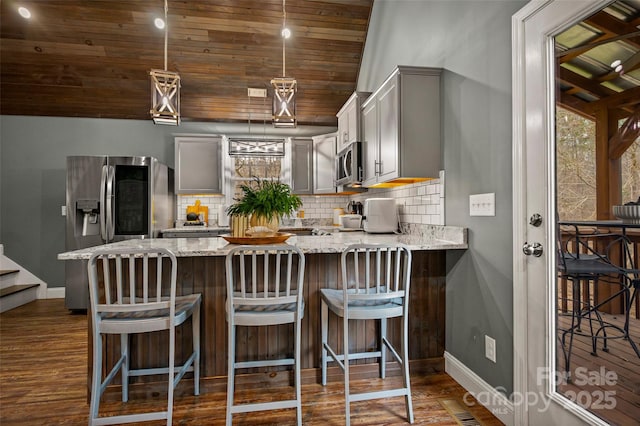 kitchen featuring dark wood finished floors, light stone counters, decorative backsplash, a peninsula, and stainless steel appliances