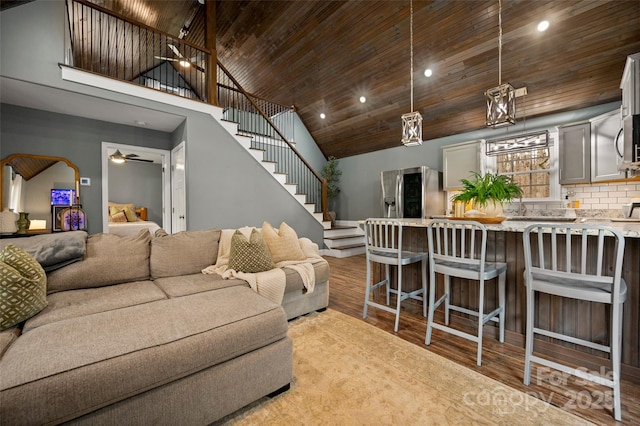 living area featuring high vaulted ceiling, a ceiling fan, wood finished floors, stairway, and wooden ceiling