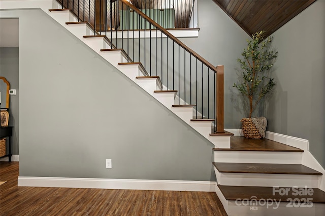 stairs featuring wood finished floors, baseboards, and a towering ceiling