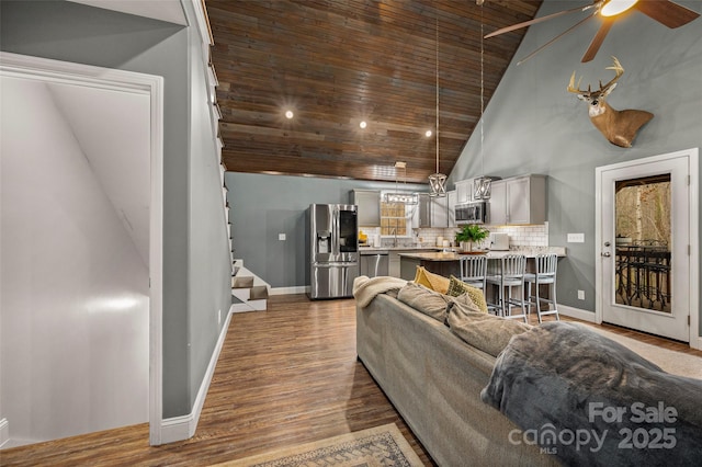 living area featuring high vaulted ceiling, dark wood-type flooring, a ceiling fan, stairway, and baseboards